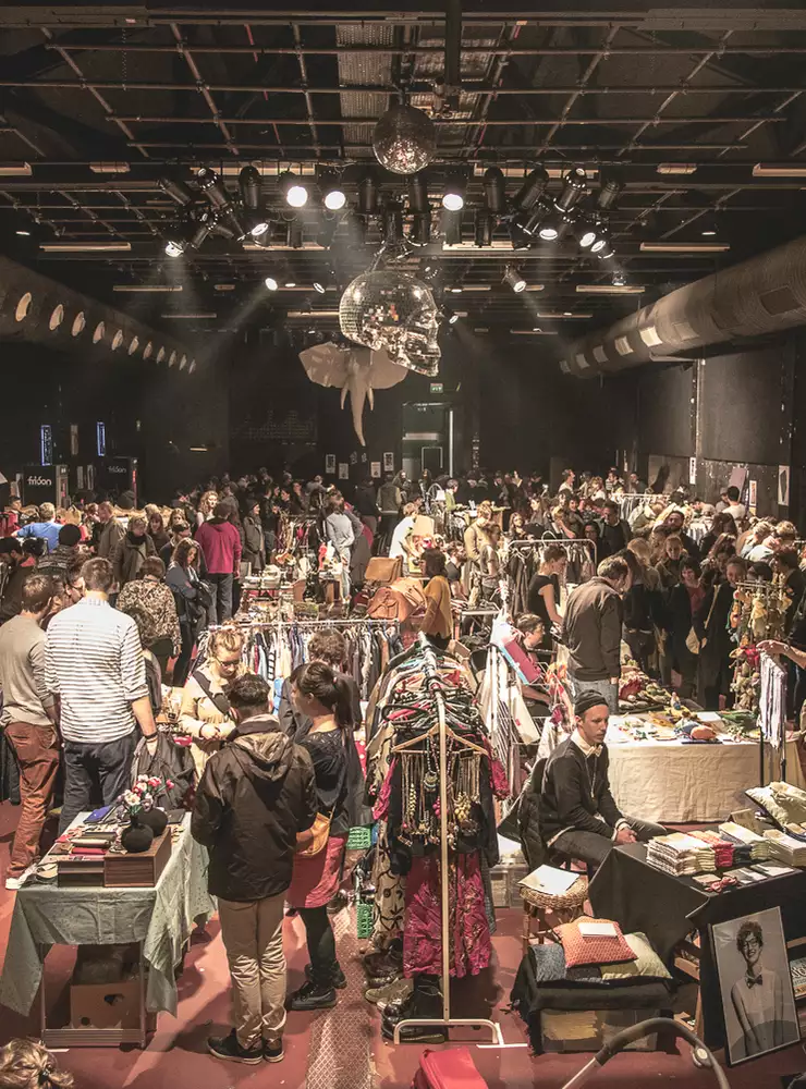 La grande salle est remplie de stands de marché aux puces. Le public flâne et regarde. 