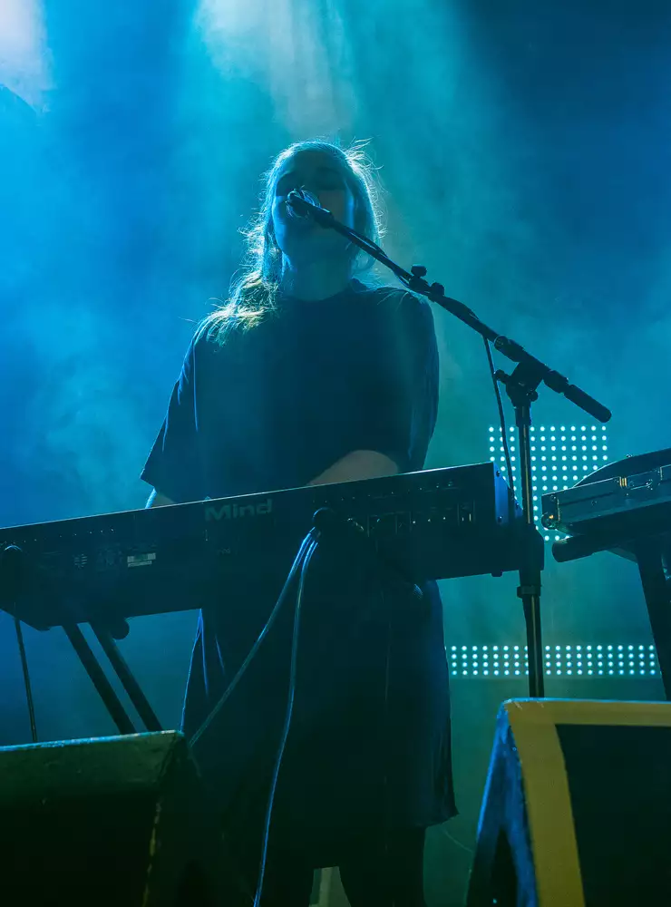 Une femme se tient derrière son clavier et chante, les yeux fermés. 